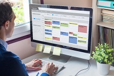 Person looking at a calendar filled with multicolored tasks on their computer.