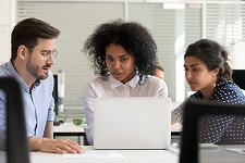 Several employees of different racial backgrounds collaborating around a computer.